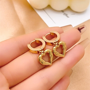 Macro shot of gold heart dangle hoop earrings held against a soft fabric background