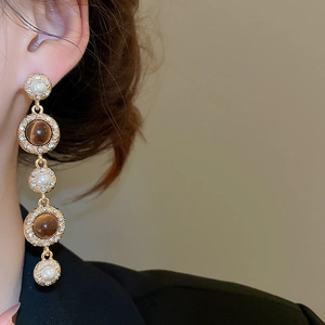 Detailed view of long gold drop earring with tiger eye stones and pearls on model