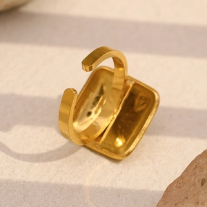 Macro detail of 18K gold plated square green stone ring on sandy textured surface
