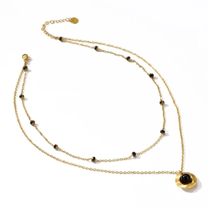 Double layered gold necklace featuring black beads and a textured sunburst disc pendant