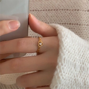 Golden heart-shaped ring with woven band and centered zircon stone on a hand