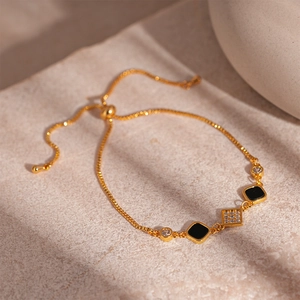 Detail of adjustable gold-plated chain bracelet with zircon square and black enamel charm