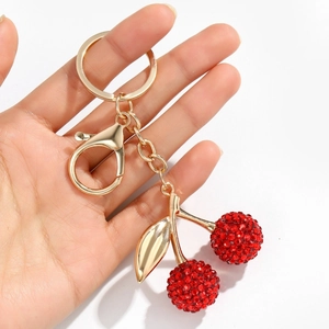 Porte-clés cerise rouge étincelant avec feuilles dorées et strass tenu dans une main