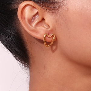 Close-up of golden hollow heart stud earring worn on ear showing polished metal finish
