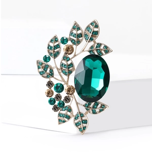 Elegant gold brooch with large oval green crystal and champagne rhinestones on white base