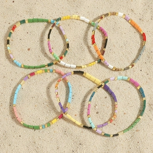 Colorful Tila bead stretch bracelet set with gold spacers on a beach sand background