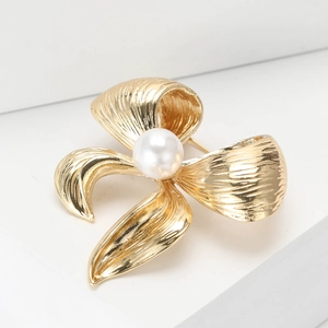 Elegant gold bow brooch with pearl inlay on minimalist white display stand