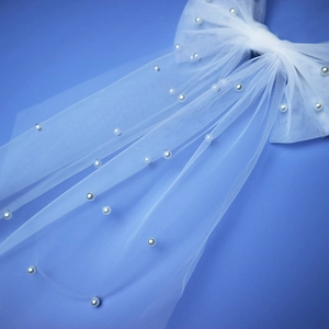 Close-up of white mesh bow hair clip with elegant pearl detailing for bridal veils