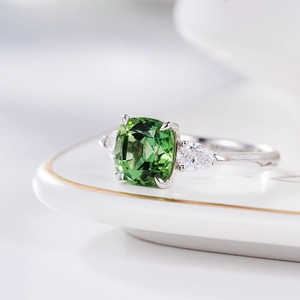 Macro shot of green emerald-cut gemstone ring on white plate with silver metal band