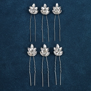 Detail of six silver leaf rhinestone hair pins arranged neatly on a dark blue velvet surface