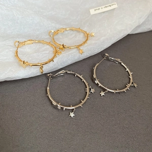 Detailed shot of gold and silver spiked hoop earrings with star pendants on textured backdrop