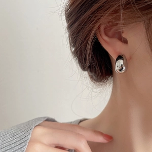 Close-up of minimalist silver boat-shaped metal stud earrings worn by a model