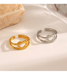 Detail of gold and silver layered rings with a knotted heart design on a textured surface
