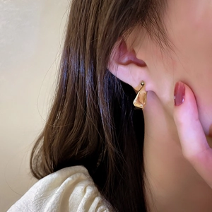 Close-up of irregular gold geometric earrings with textured metallic finish on model