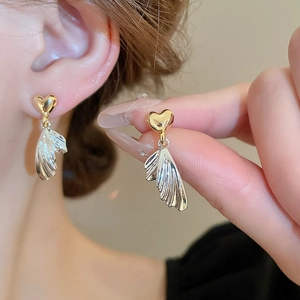 Elegant gold heart and textured silver wing tassel earrings worn by a model