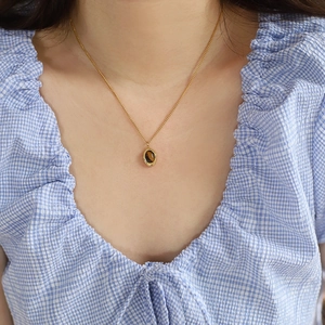 Close-up of a tiger eye gemstone necklace worn against a blue and white plaid shirt