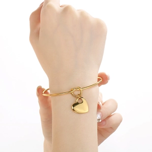 Minimalist gold stainless steel knot bangle featuring a smooth heart-shaped pendant charm
