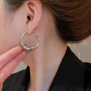 Close-up of irregular silver wave hoop earrings on model for a stylish aesthetic