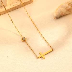 Détail d'un collier croix en acier doré avec gemme sertie sur fond de cuir élégant