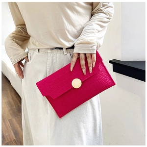 Detail of rose pink crocodile pattern envelope clutch with large golden round buckle closure