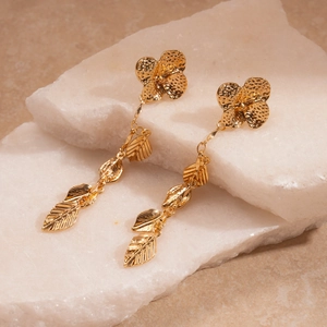 Macro shot of gold metallic flower and leaf tassel earrings on natural white stone base