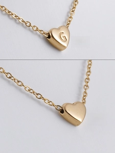 Détail recto verso d'un collier pendentif cœur doré avec la lettre G gravée dessus
