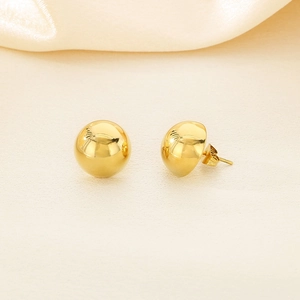 Macro detail of polished gold spherical stud earrings on silky beige fabric background