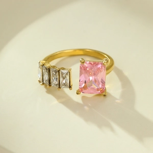 Detail of gold open ring featuring large pink rectangular gemstone and clear zircon accents