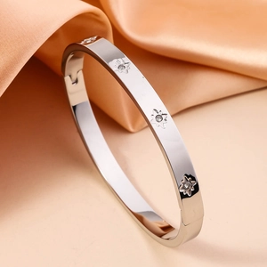 Detail of silver stainless steel bangle with flower engraving and diamonds on satin
