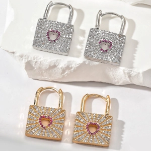 Gold and silver heart lock earrings with red zircons on white textured stone base