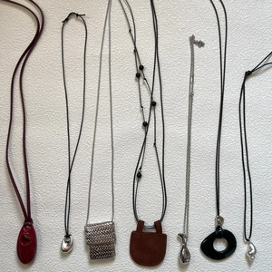 Collection of seven minimalist leather and metal pendant necklaces on a white background