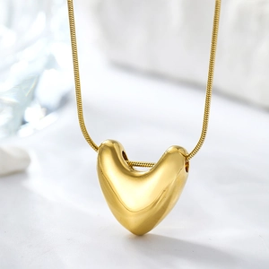 Close-up of polished gold heart pendant with sleek snake chain on white stone surface