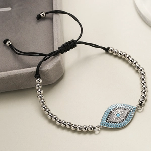 Detail of silver beaded evil eye bracelet with blue zircon and black cord on jewelry tray