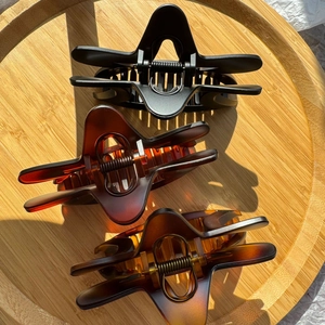 Three large star-shaped hair claws in matte black and amber brown on a wooden tray