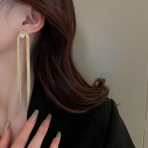 Detail of long gold tassel earrings with pearls worn with an elegant black suit