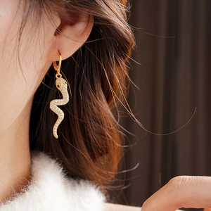 Close-up of gold-plated snake earrings with sparkling cubic zirconia on model's ear