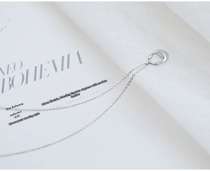 Close-up of minimalist silver water drop necklace on a soft white fabric background