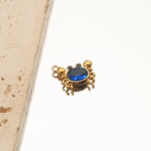 Close-up of golden crab pendant featuring a central blue gemstone on reflective surface