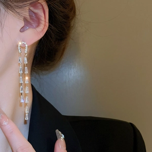Macro shot of gold long tassel earrings with rectangular crystals on a female model