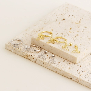 Detailed display of S925 silver bow earrings in gold and silver on textured stone plates