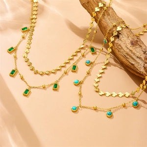Detail showing layered gold necklaces with turquoise and green stones on a wooden block