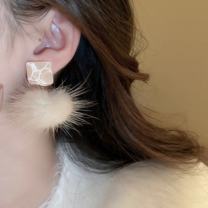Close-up of model wearing stylish cream resin earrings with soft white plush pom-poms