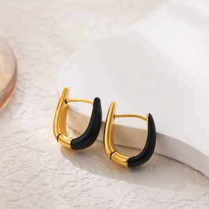 Macro detail of U-shaped gold earrings with black enamel finish on stone base