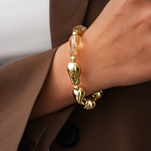 Close-up of irregular amber acrylic and gold metallic beaded bracelet on a wrist