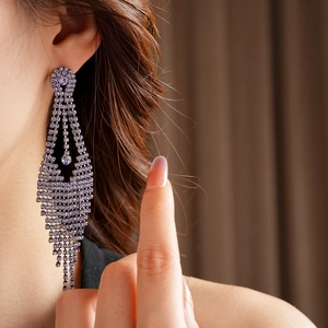 Gros plan de boucles d'oreilles à pompons violets et cristaux portées par un mannequin