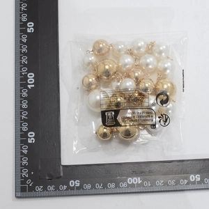 Detail showing oversized gold beads and white faux pearls next to a size measuring scale