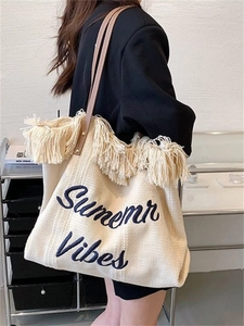 Detailed side view of cream woven tote bag with fringe, Summer Vibes embroidery and leather straps