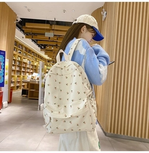 Detail of floral canvas backpack in cream white, shown on model in a cozy bookstore setting