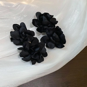 Détail des boucles d'oreilles fleurs en satin noir faites main sur fond de soie blanche