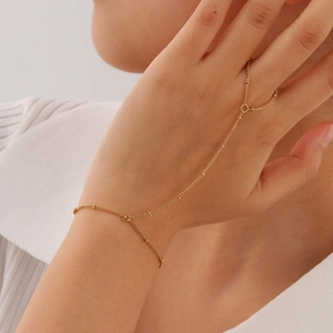 Detail of a gold stainless steel finger bracelet featuring fine bead chains on a hand
